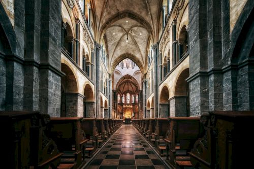 The image shows the interior of a grand Gothic cathedral with high vaulted ceilings, elaborate columns, and ornate seating areas leading to an altar.