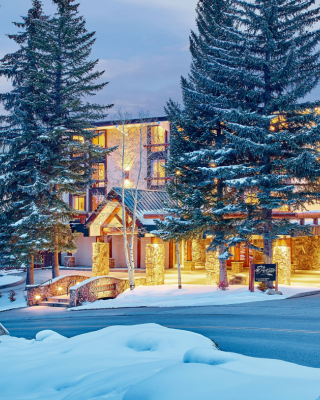 The image shows a cozy hotel surrounded by snow-covered trees, illuminated in warm light, creating a winter wonderland atmosphere.