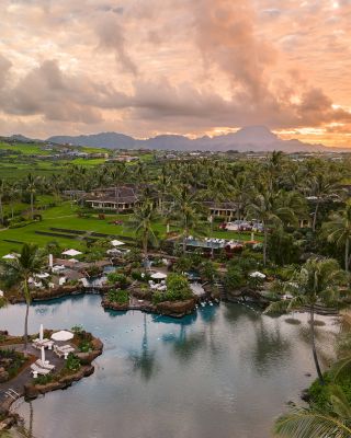 A scenic resort with lush greenery, palm trees, a tranquil lagoon, and a beautiful sunset in the background creates a serene atmosphere.