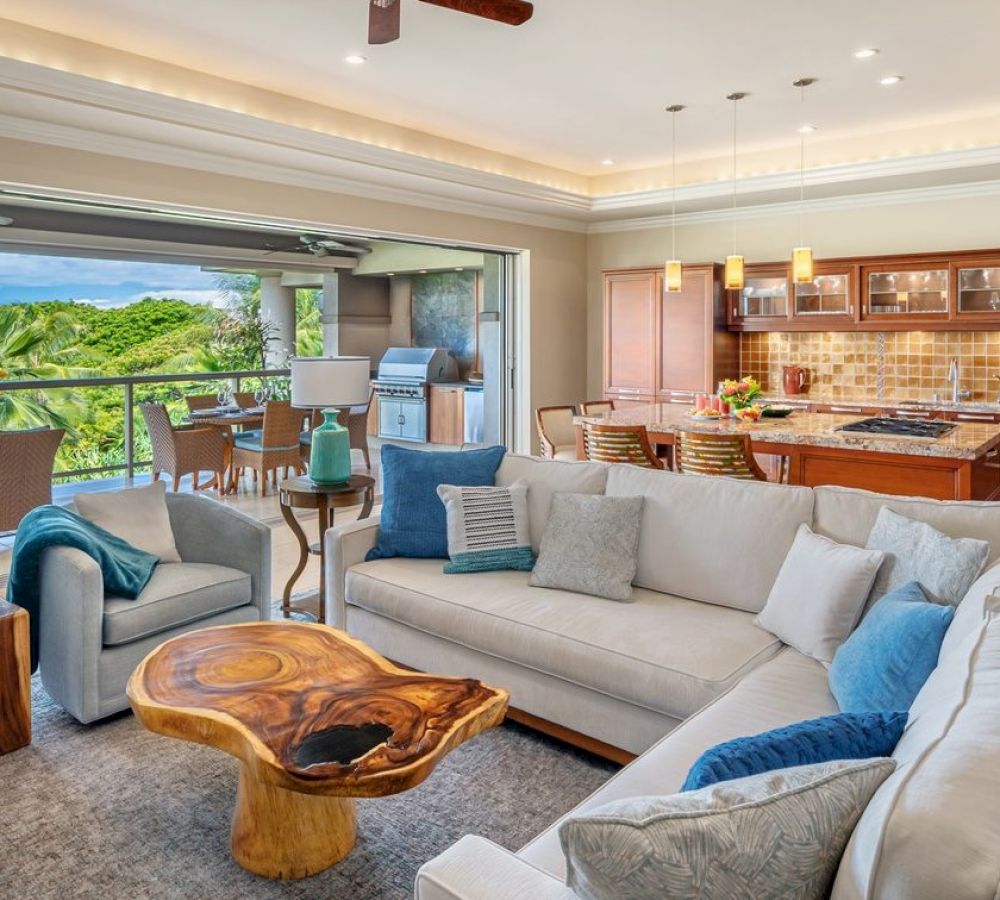 A modern living room with a white sofa, wooden coffee table, open kitchen, and outdoor patio with seating and a barbecue grill.