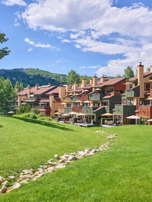 The image shows a scenic view of colorful buildings lined up against a backdrop of greenery and blue skies with fluffy clouds.