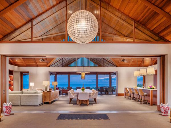 Spacious open-concept living and dining area with wooden ceilings, a large globe chandelier, and a view of the ocean through wide glass doors.