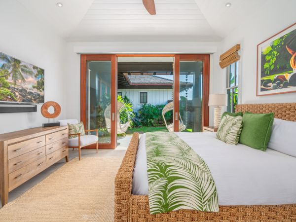 A tropical-themed bedroom with a wicker bed, green accents, large sliding glass doors, a TV, and wooden furniture leading to an outdoor area.