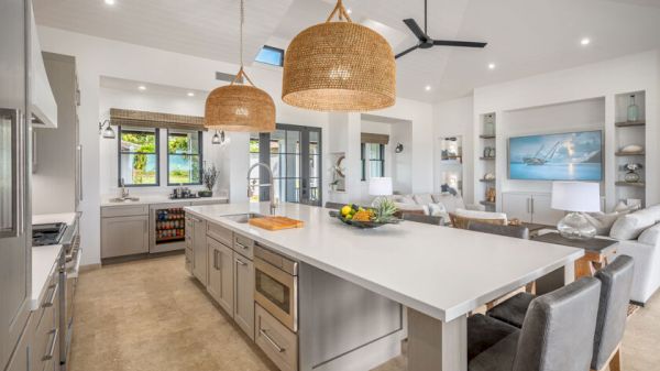 A modern open-concept kitchen and living area with a large island, pendant lights, and cozy seating, featuring neutral tones and natural lighting.