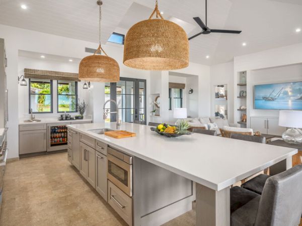 A modern open-concept kitchen and living area with a large island, pendant lights, and cozy seating, featuring neutral tones and natural lighting.