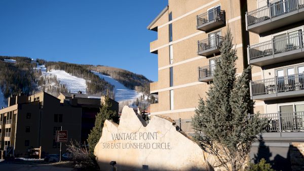 The image shows a resort sign, "Vail Point," with snowy mountains in the background and buildings nearby. It looks inviting.
