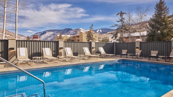 A serene outdoor pool surrounded by lounge chairs with a scenic mountain backdrop and a partly cloudy sky.