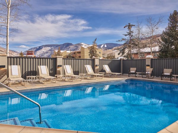 A serene outdoor pool surrounded by lounge chairs with a scenic mountain backdrop and a partly cloudy sky.