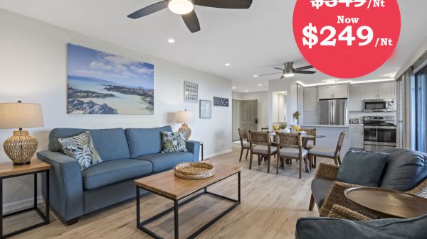 The image shows a modern living space with a sofa, dining area, and kitchen, featuring a price drop for accommodation.