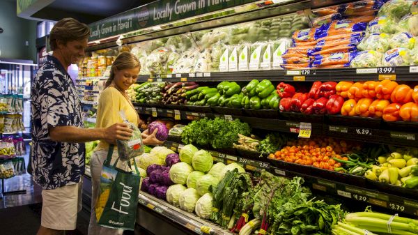 A couple shops for fresh produce in a colorful grocery store, exploring vibrant vegetables and fruits together.