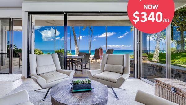 A modern living room with large windows overlooking the ocean, featuring white chairs, a round coffee table, and a discount sign showing the price drop.