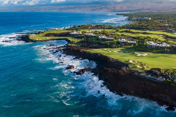 The image showcases a stunning coastal landscape with a golf course, rocky shores, and vibrant blue waters under a clear sky.