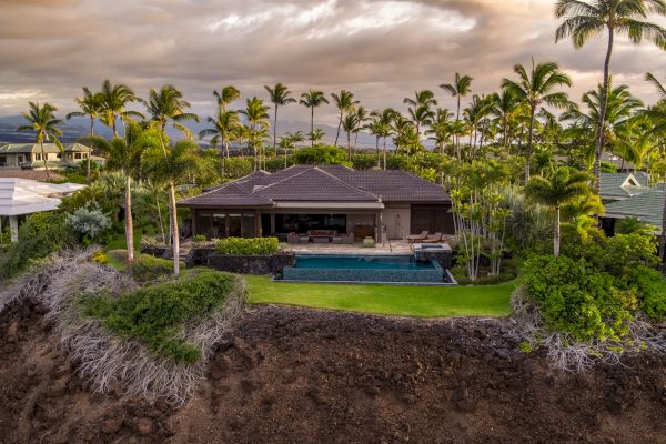 The image showcases a beautiful tropical home with a pool, surrounded by lush palm trees and a dramatic cliff view.