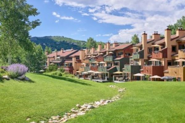 The image features a row of colorful buildings set against a lush green landscape, with a clear sky and a small stone path.