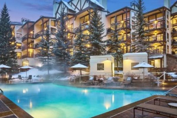 The image shows a snowy resort with a heated pool, surrounded by tall trees and mountains, creating a cozy winter atmosphere.