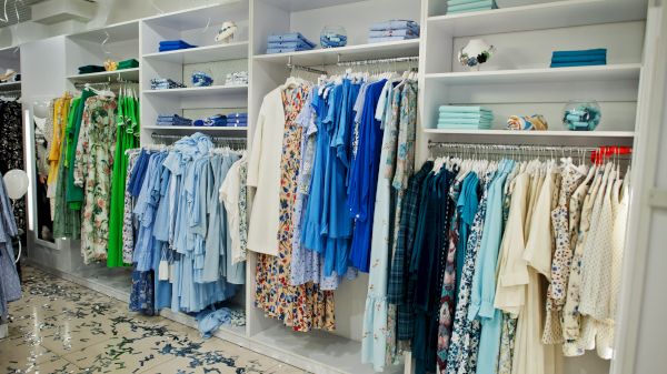 The image shows a clothing store with shelves displaying a variety of colorful garments, primarily in blue and green hues.