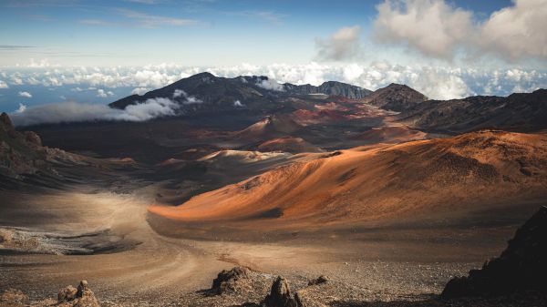The image showcases a stunning volcanic landscape with rugged terrain, vibrant orange and brown colors, and a dramatic sky above.