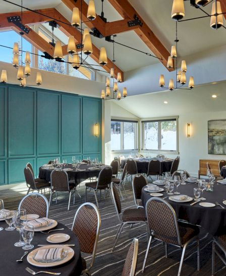 The image shows a well-decorated dining area with elegantly set tables, modern lighting, and large windows offering natural light.