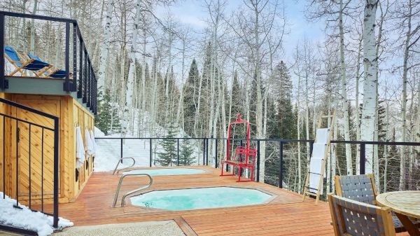 The image features a cozy outdoor deck with a hot tub surrounded by trees, perfect for relaxation in a snowy setting.