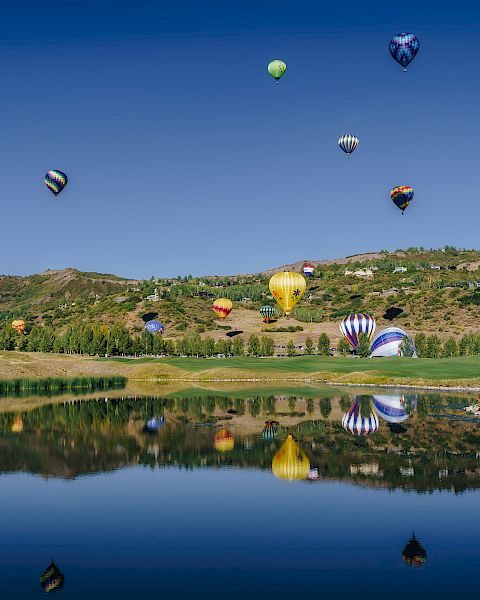 The image showcases colorful hot air balloons floating over a serene landscape, reflected in a calm body of water below.