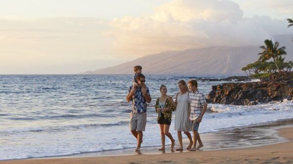 A family walks along a beach at sunset, enjoying the ocean view and each other's company in a serene atmosphere.