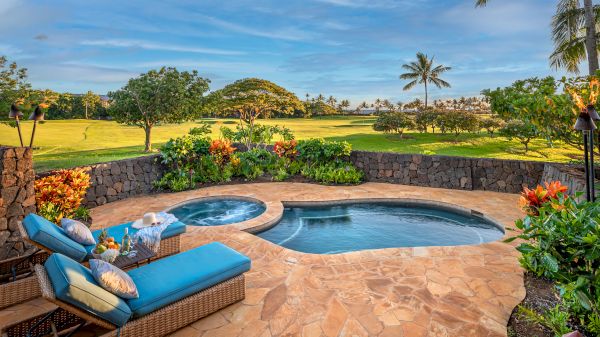The image shows a serene outdoor area with a pool, spa, lounge chairs, and vibrant flowers, set against a lush landscape.