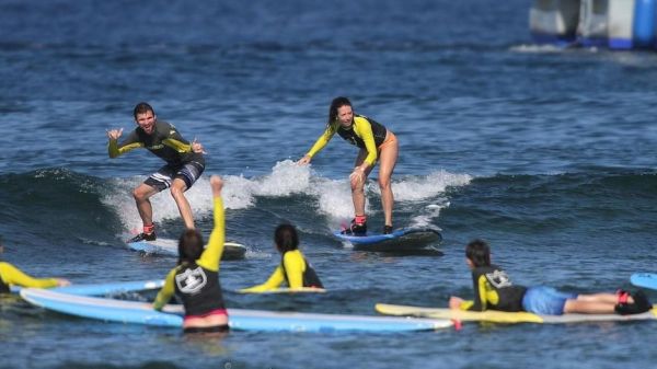 The image shows surfers in action, with some riding waves and others on surfboards, engaged in a sunny beach setting.
