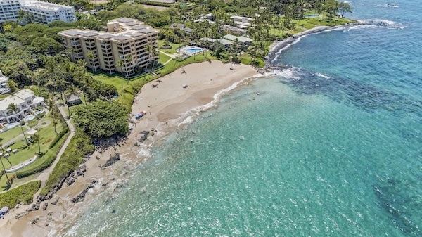 The image shows a coastal area with sandy beaches, lush greenery, and buildings near the shore, creating a vibrant seaside scene.