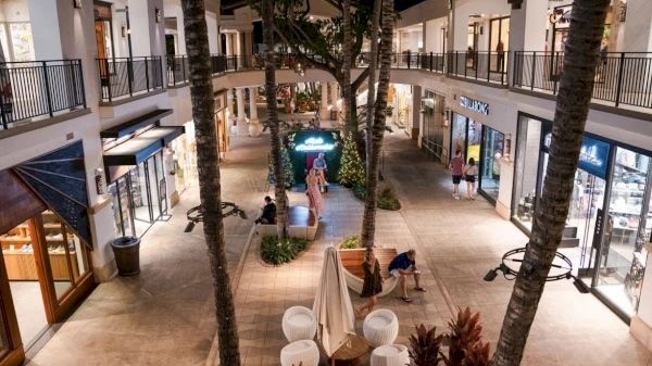 The image shows a beautifully lit outdoor shopping area at night, featuring stores and lush greenery. It's inviting and serene.