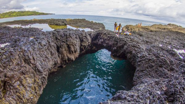 The image features rocky coastal formations with a deep pool of water, and people exploring the scenic shoreline.