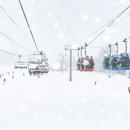 The image shows a snowy landscape with ski lifts and skiers amidst falling snow, creating a winter wonderland scene.