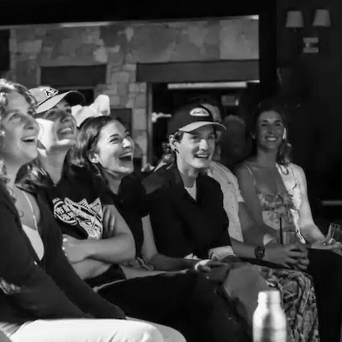 The image shows a group of people sitting together, laughing and enjoying a moment, likely at an event or performance.