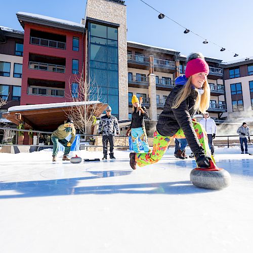 A girl curls on ice in colorful pants while others enjoy the sport in a sunny, modern outdoor setting. Winter fun abounds.