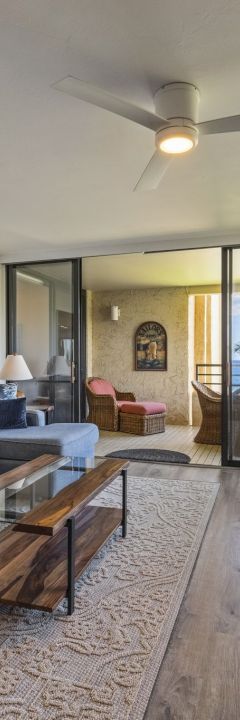 The image shows a stylish living room with a sea view, featuring a couch, coffee table, dining area, and large windows.