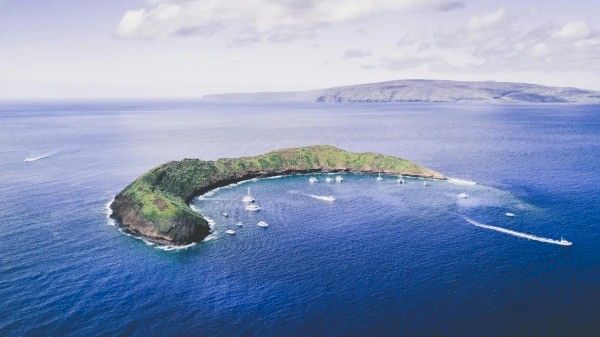 The image shows a lush, green island surrounded by clear blue waters, with boats navigating around its shores. It looks serene.