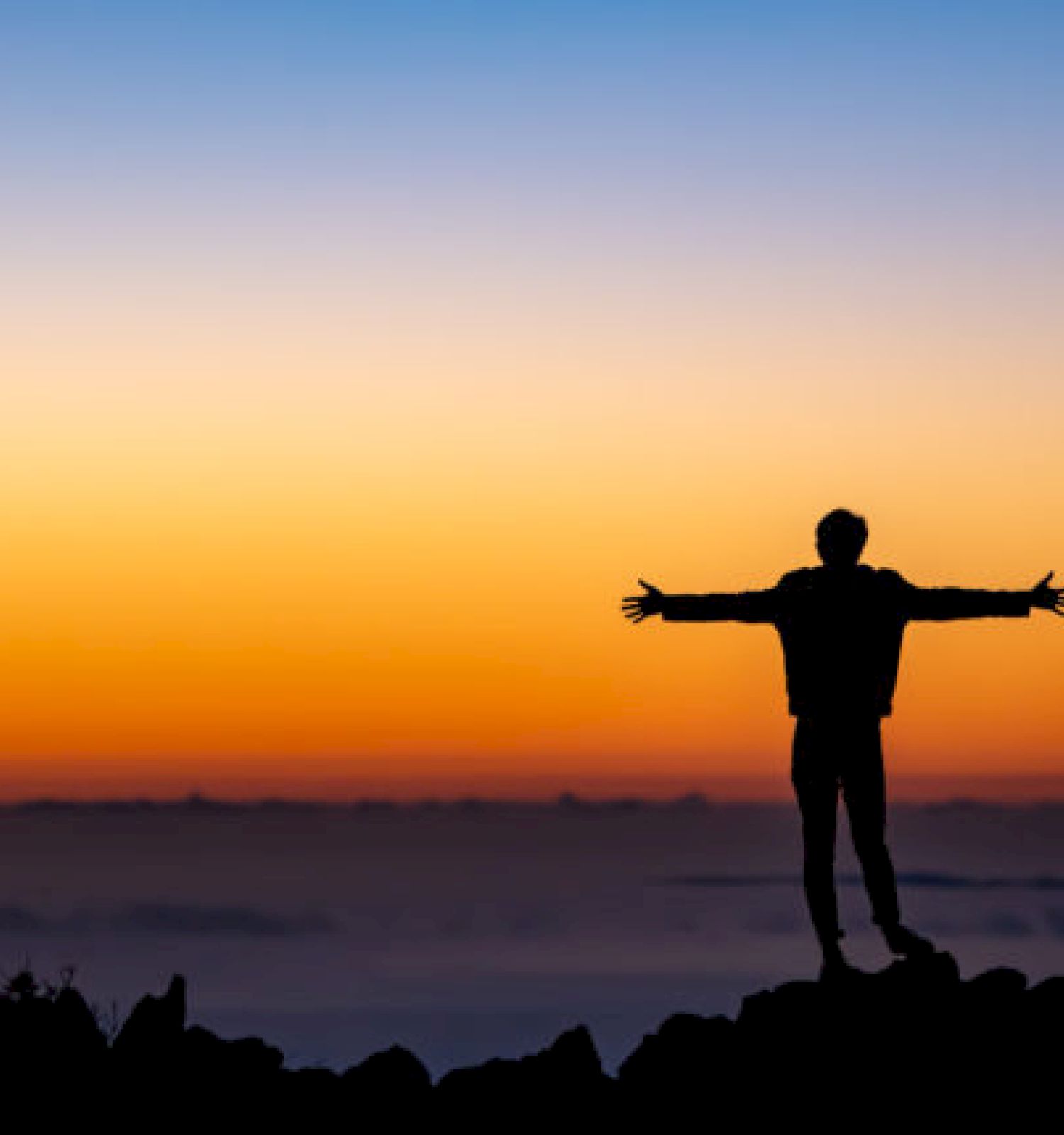 A silhouetted figure stands on a rock, arms outstretched against a vibrant sunset sky, conveying a sense of freedom and serenity.