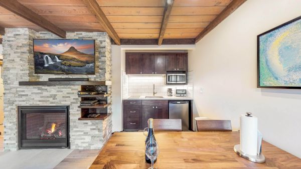 A cozy room with a fireplace, TV, and a small kitchen area. A table with a wine bottle and paper towels is in the foreground.