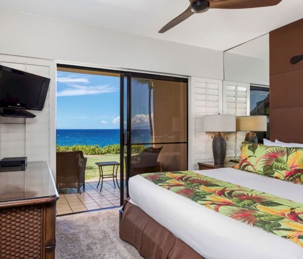 The image shows a bedroom with tropical decor, a view of the ocean, and a balcony. It's a cozy space for relaxation.