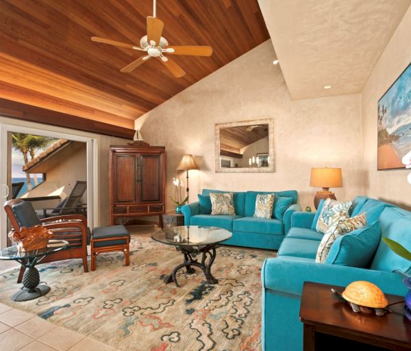 The image features a bright, coastal living room with turquoise furniture, wooden accents, and a stunning ocean view.