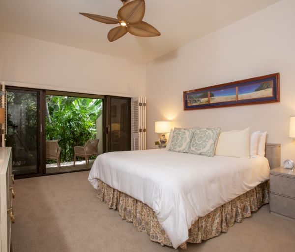 The image shows a bright bedroom with a large bed, two bedside lamps, a ceiling fan, and a view of greenery outside.