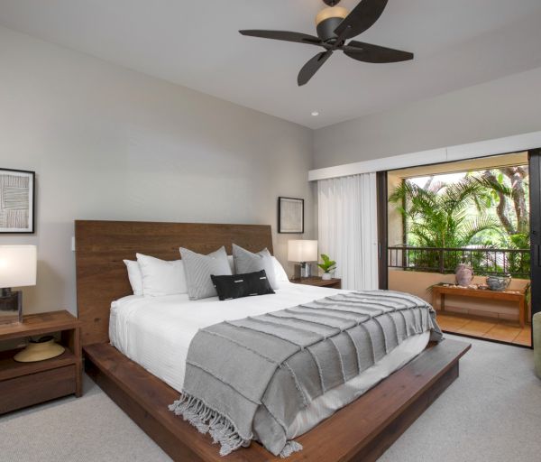 The image shows a modern bedroom with a large bed, wooden furniture, and a balcony overlooking greenery. It's cozy and inviting.