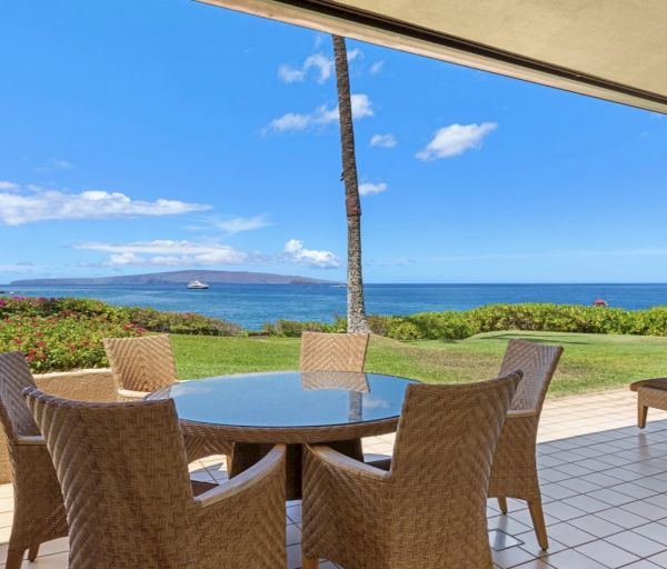 The image shows a scenic view from a patio with wicker furniture overlooking a calm sea and blue sky. It's quite relaxing.