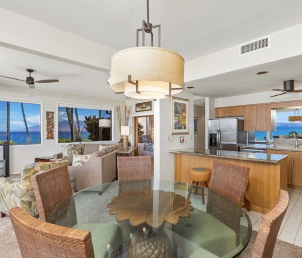 The image features a modern open-concept living space with a dining area, kitchen, and scenic ocean view through large windows.