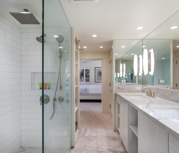 The image shows a modern bathroom with a glass shower, dual sinks, and ample mirrors, creating a spacious and bright atmosphere.