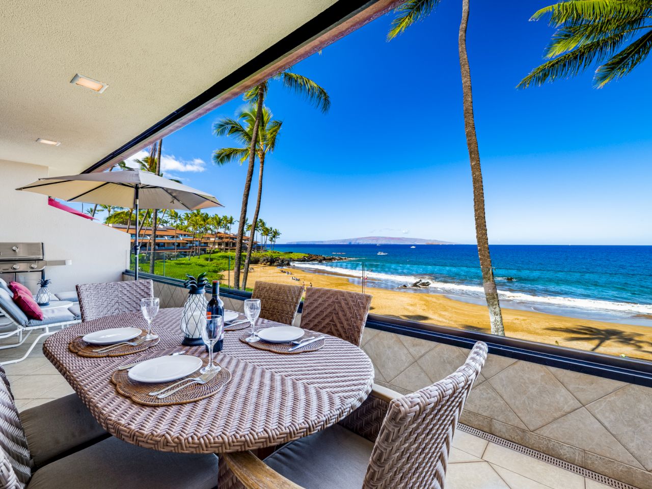 The image shows a beautiful beachfront patio with a dining set, overlooking a serene beach and clear blue sky. Relaxing vibes.