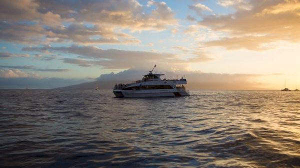 A boat sails on calm waters at sunset, with beautiful clouds and a distant landmass creating a serene coastal scene.