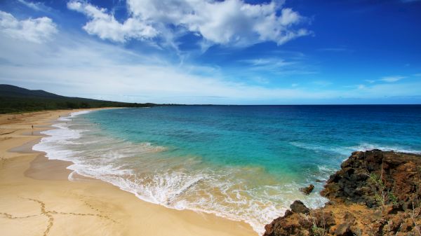 A serene beach scene featuring soft sand, clear turquoise waters, and rocky formations under a bright blue sky. It's picturesque.