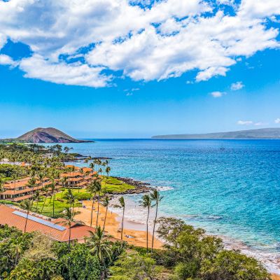 The image shows a scenic coastal view with turquoise water, lush green landscape, and a clear blue sky. It&rsquo;s quite picturesque.