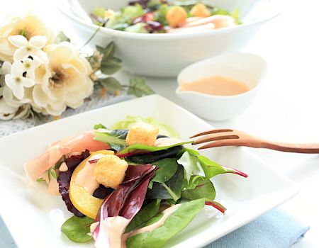 A fresh salad with greens, fruits, and a dressing, served alongside a larger bowl and some decorative flowers. Enjoy the meal.