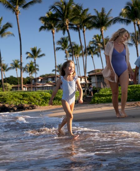 Children and adults walk along a sunny beach with palm trees, waves lapping at shore, vacation vibe, blue skies, family enjoying.